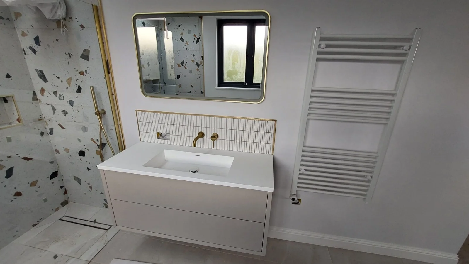 Terrazzo-tiled shower beside a vanity with brushed brass taps